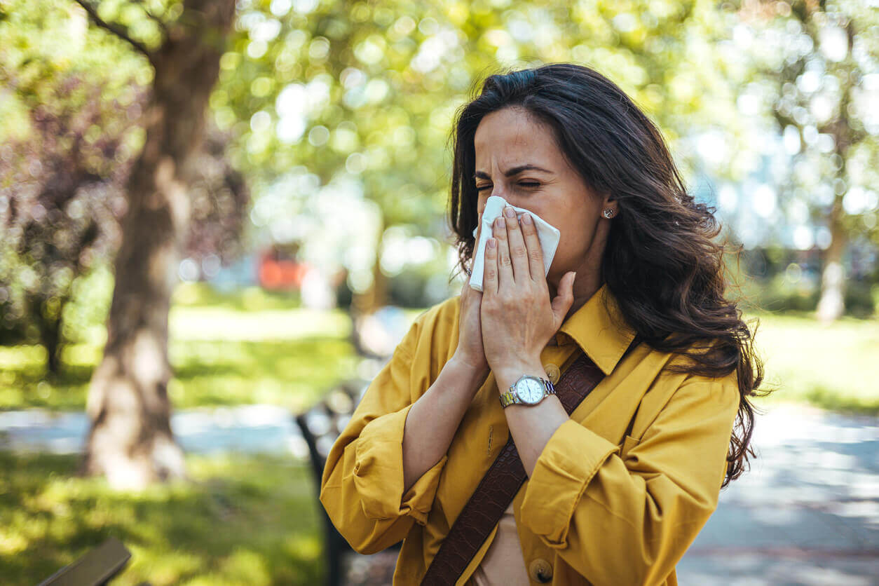 Image of a woman in a yellow top blowing her nose due to an allergic asthma attack.