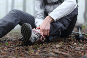 A hiker is sitting on the ground alone in the mountain with a sprained ankle.