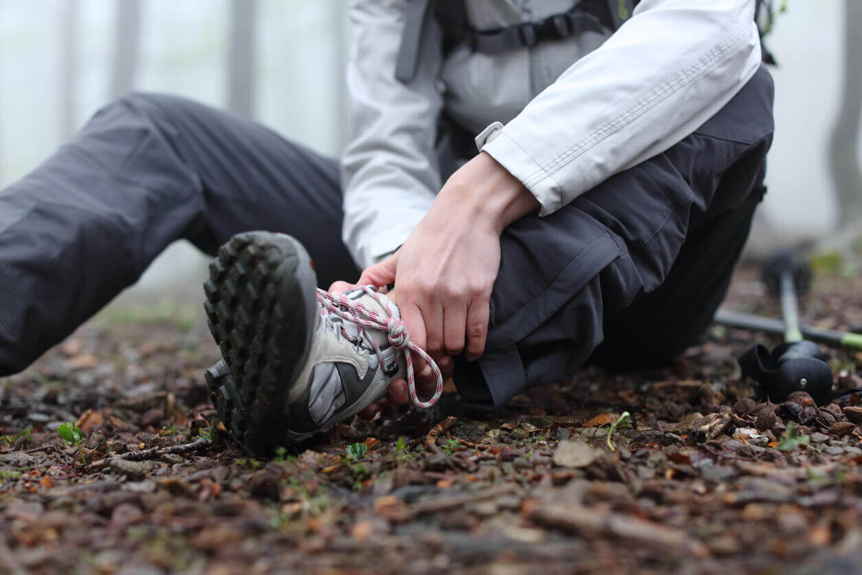 A hiker is sitting on the ground alone in the mountain with a sprained ankle.