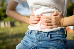 A woman with a stomach ache is experiencing pain from gastroenteritis, commonly known as the stomach bug virus, causing her to hold her stomach in discomfort.