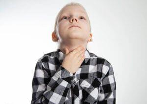 A seven-year-old girl in a checkered shirt holds her throat due to strep throat and inflammation.