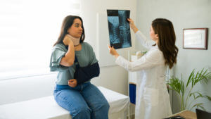 Image of a doctor showing and explaining X-ray results to a young injured patient wearing a neck brace and arm sling.