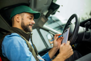 A young truck driver sits in his truck with a pen and paper during his DOT physical examination.