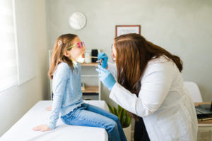 A pediatrician examines a young girl's throat for strep throat using a tongue depressor during an urgent care consultation.