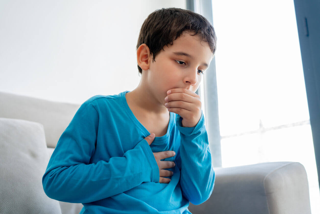 Little boy sitting on sofa at home and holding hand on chest due to an allergic asthma attack.