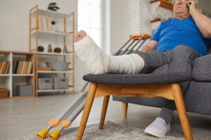 Senior man with broken leg in plaster cast sitting on couch and talking on phone.